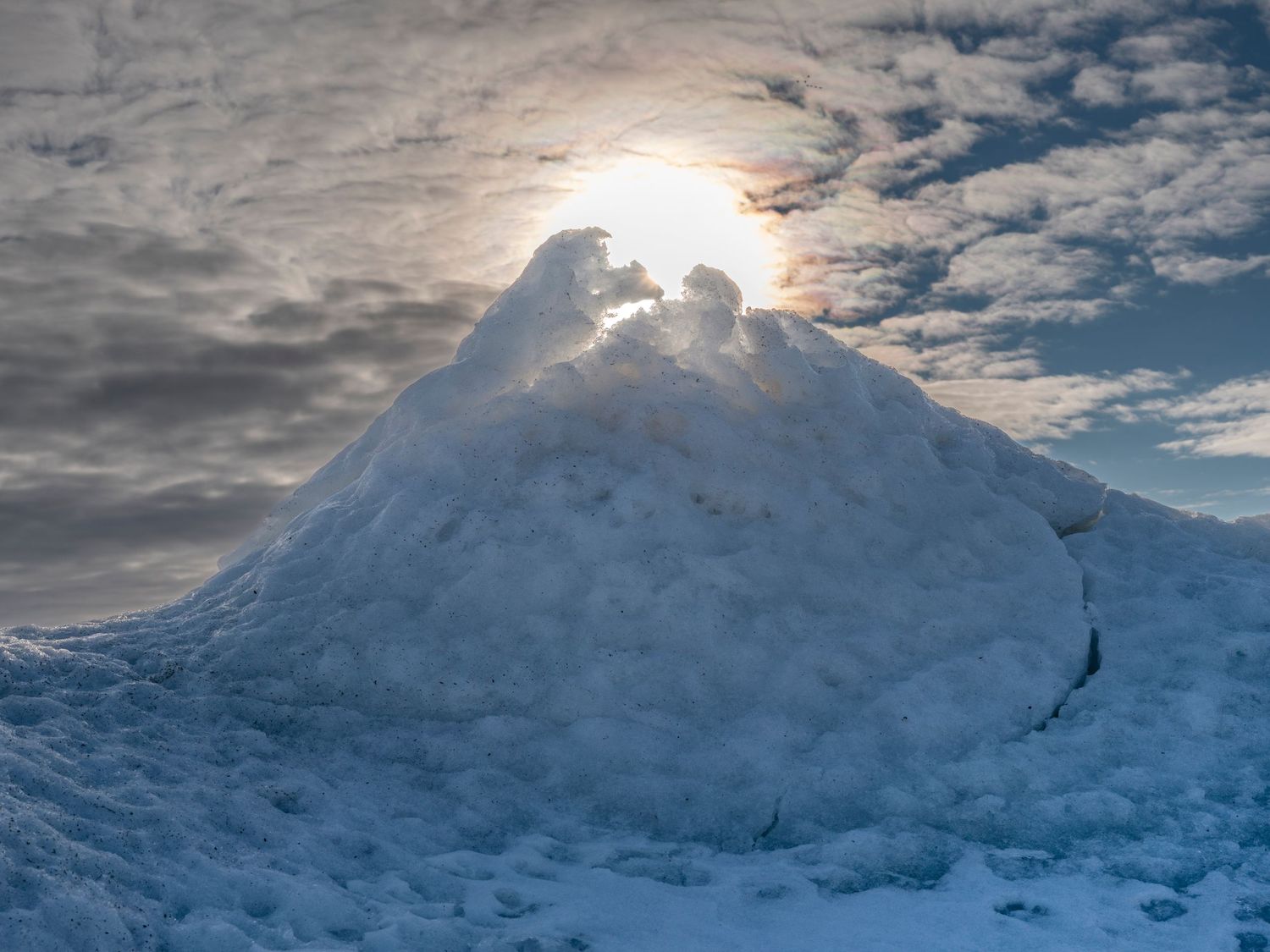 Large snow mound glowing under a dramatic cloudy sky with the sun shining behind it in winter.