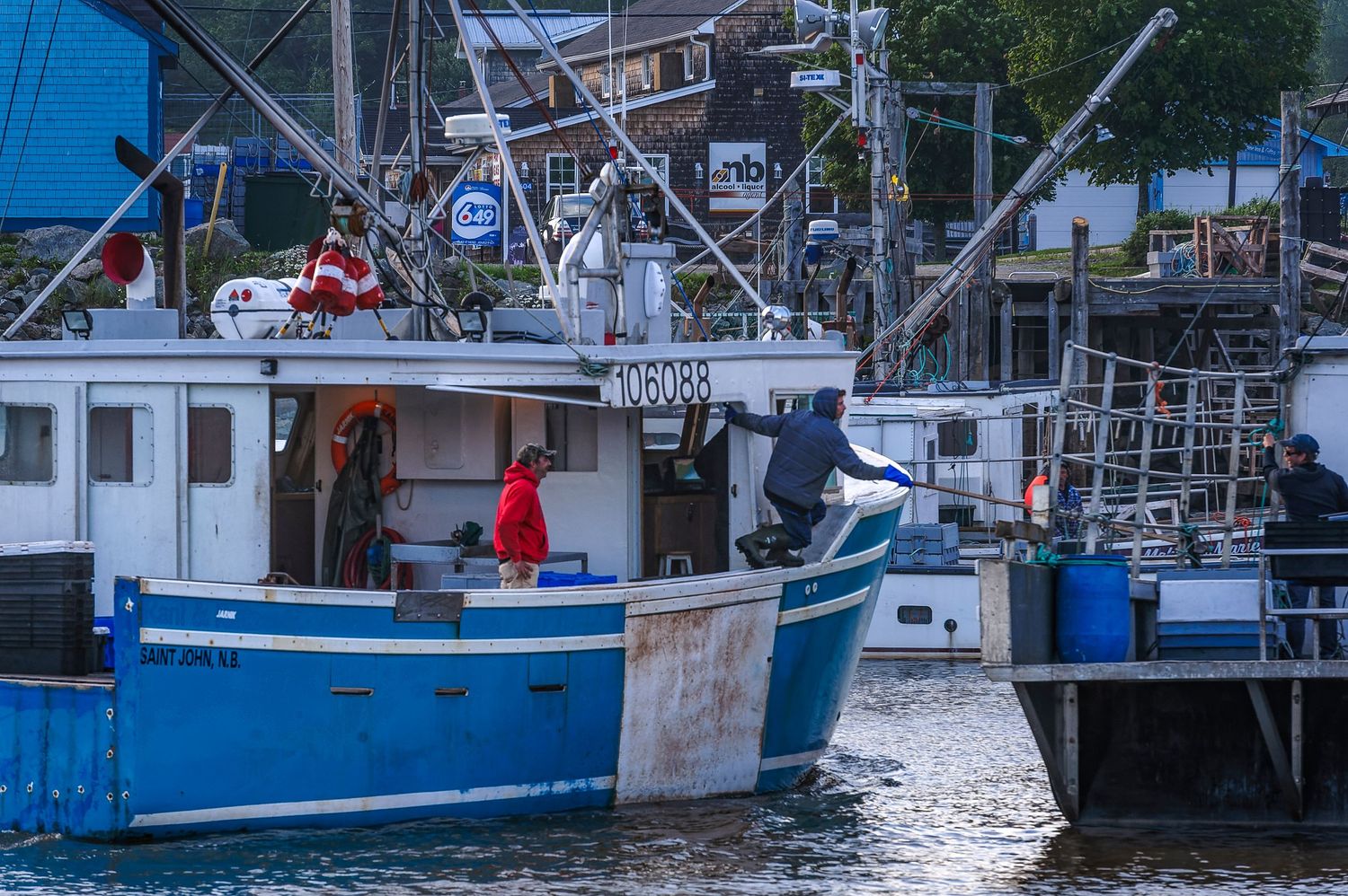 Blue fishing boat docked at a harbor pier with crew members working on deck at dusk.