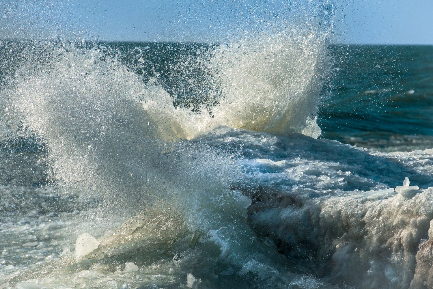 Powerful ocean waves crashing and splashing dramatically against the shore with white sea foam under bright sunlight.