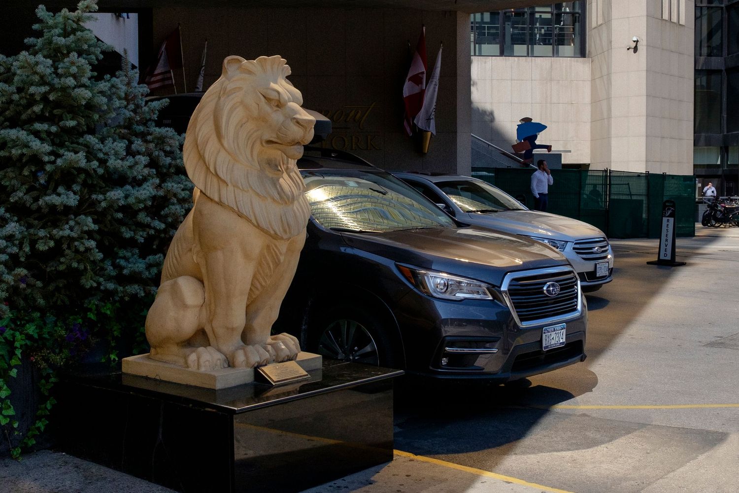 A large stone lion sculpture guards the entrance of an upscale hotel with parked cars nearby.