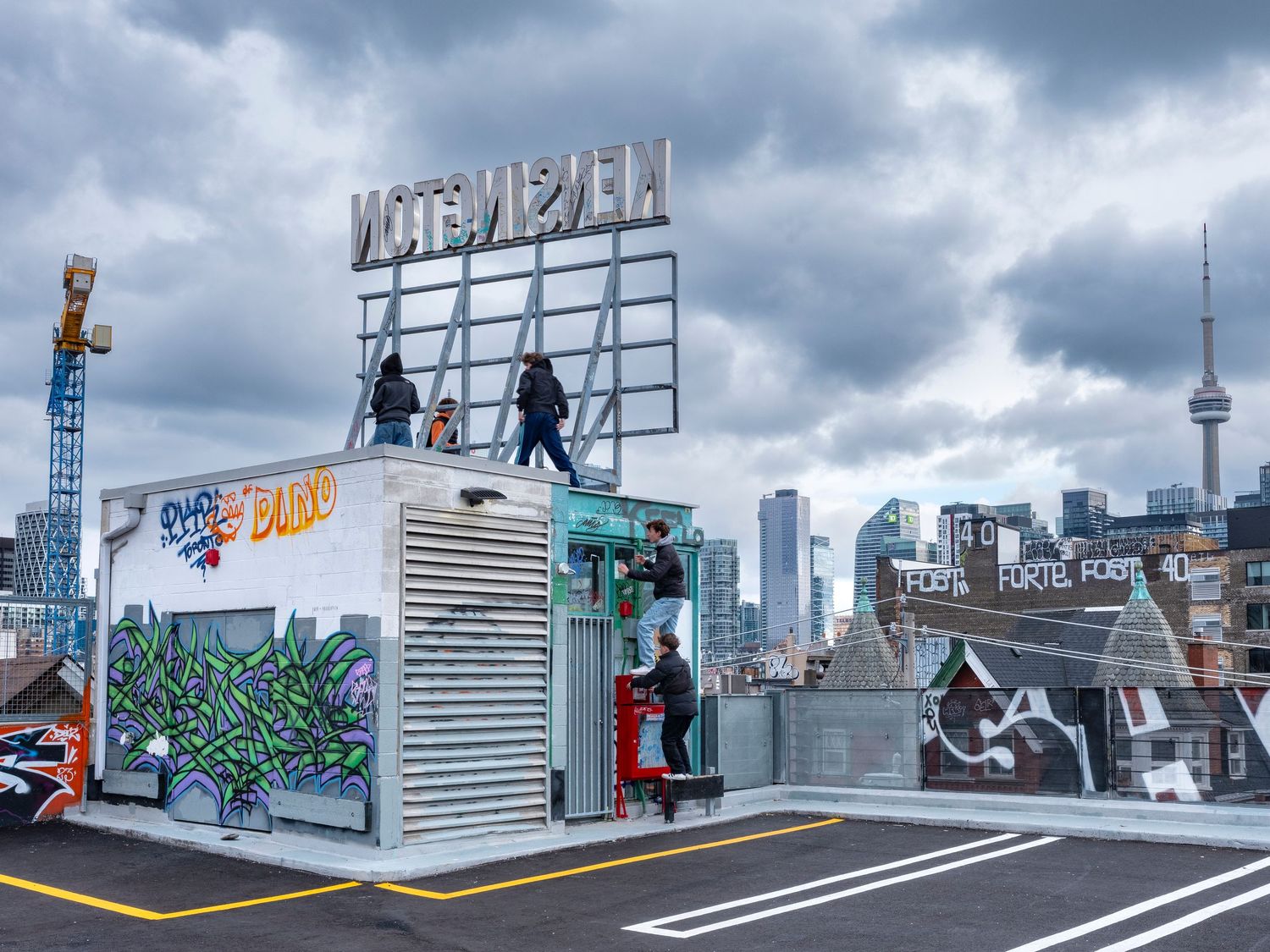 Rooftop graffiti art installation with Toronto skyline and CN Tower in background under cloudy skies.