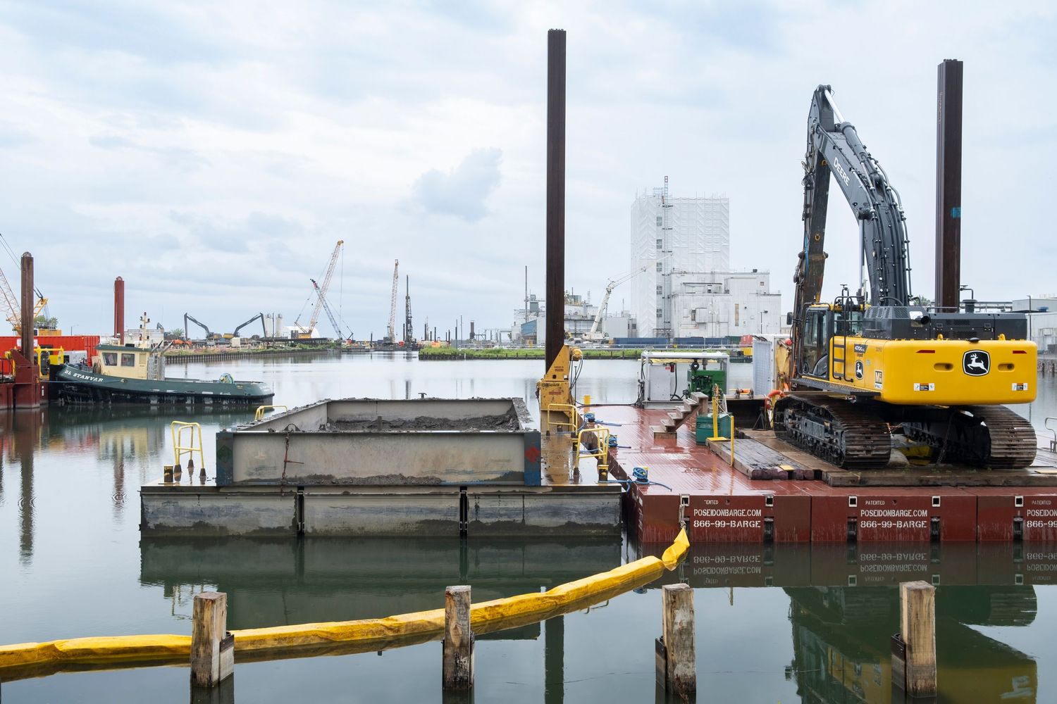John Deere excavator on a barge during waterfront construction project on an overcast day.