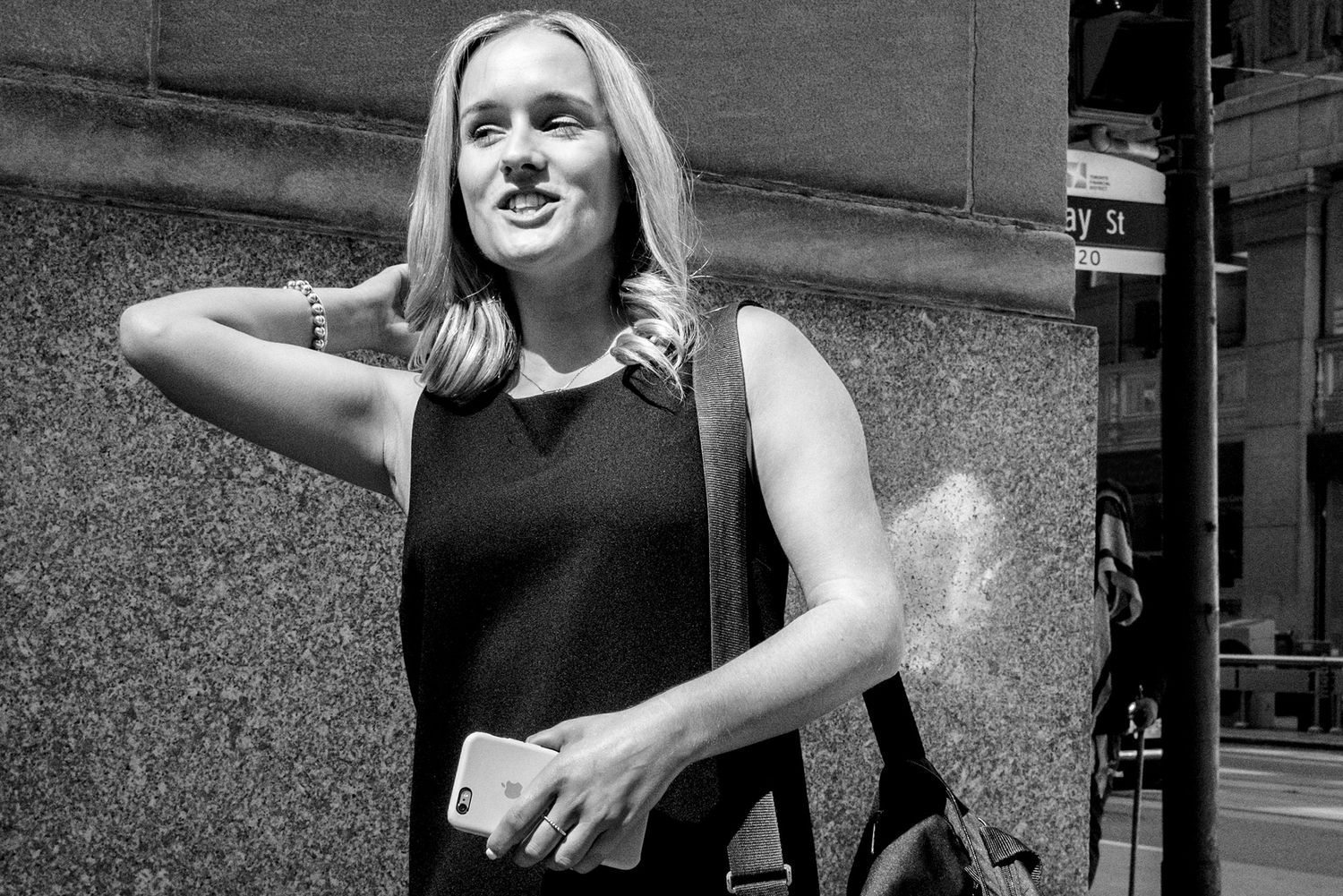 Black and white street portrait of a smiling young woman with headphones walking in a city.
