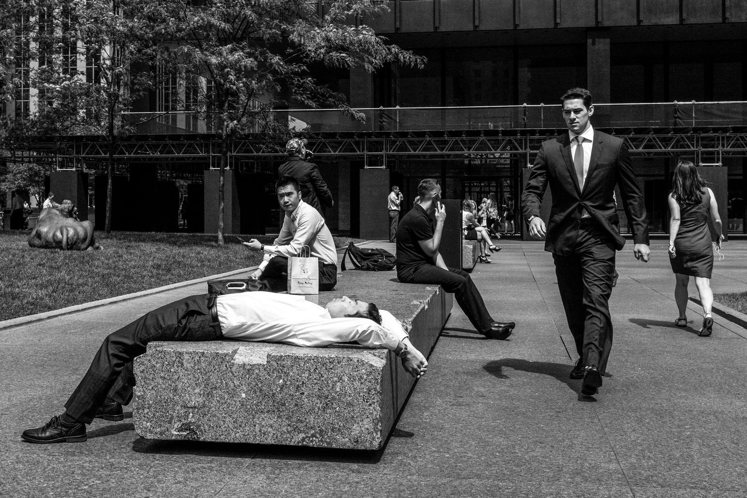 Black and white photo of businessmen in suits near stone benches outside a modern office building.