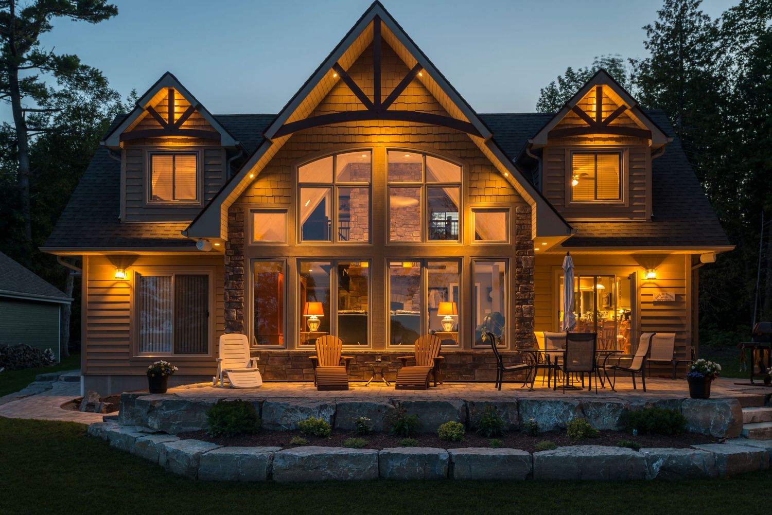 A beautifully lit craftsman-style home exterior glowing warmly at dusk with a stone patio.