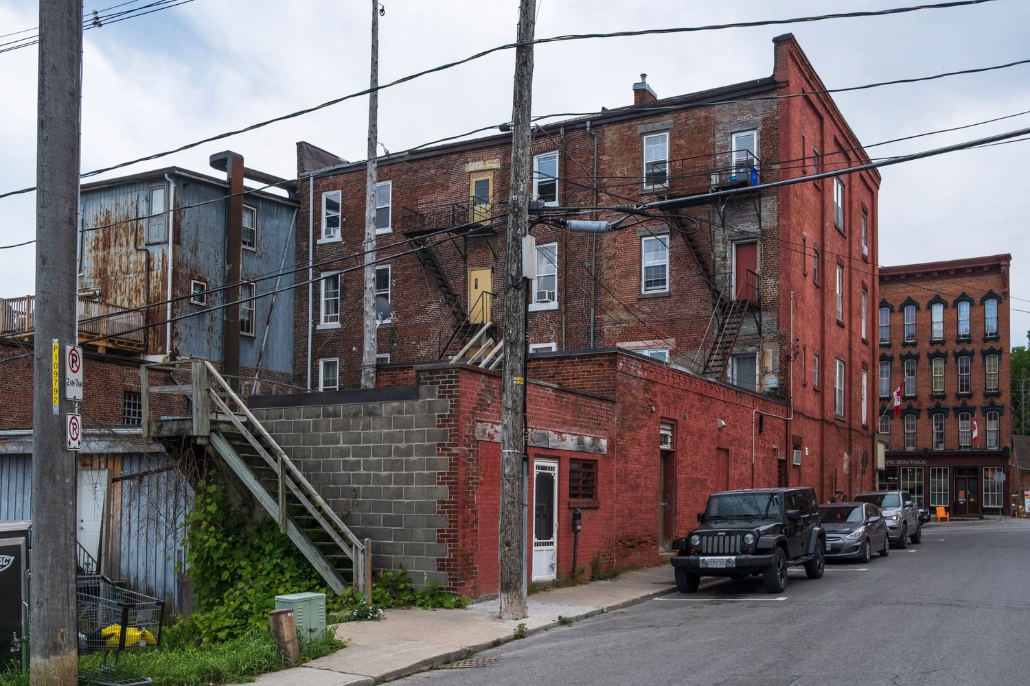 Old red brick urban buildings with fire escapes and utility poles on a city back street.
