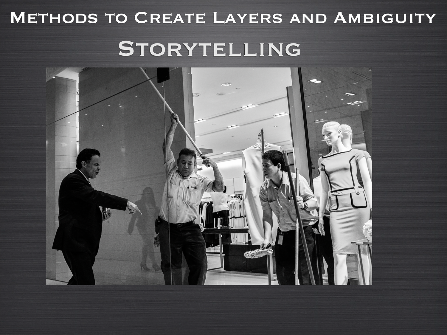 Black and white photo of workers moving mannequins outside a retail store, creating layered storytelling.