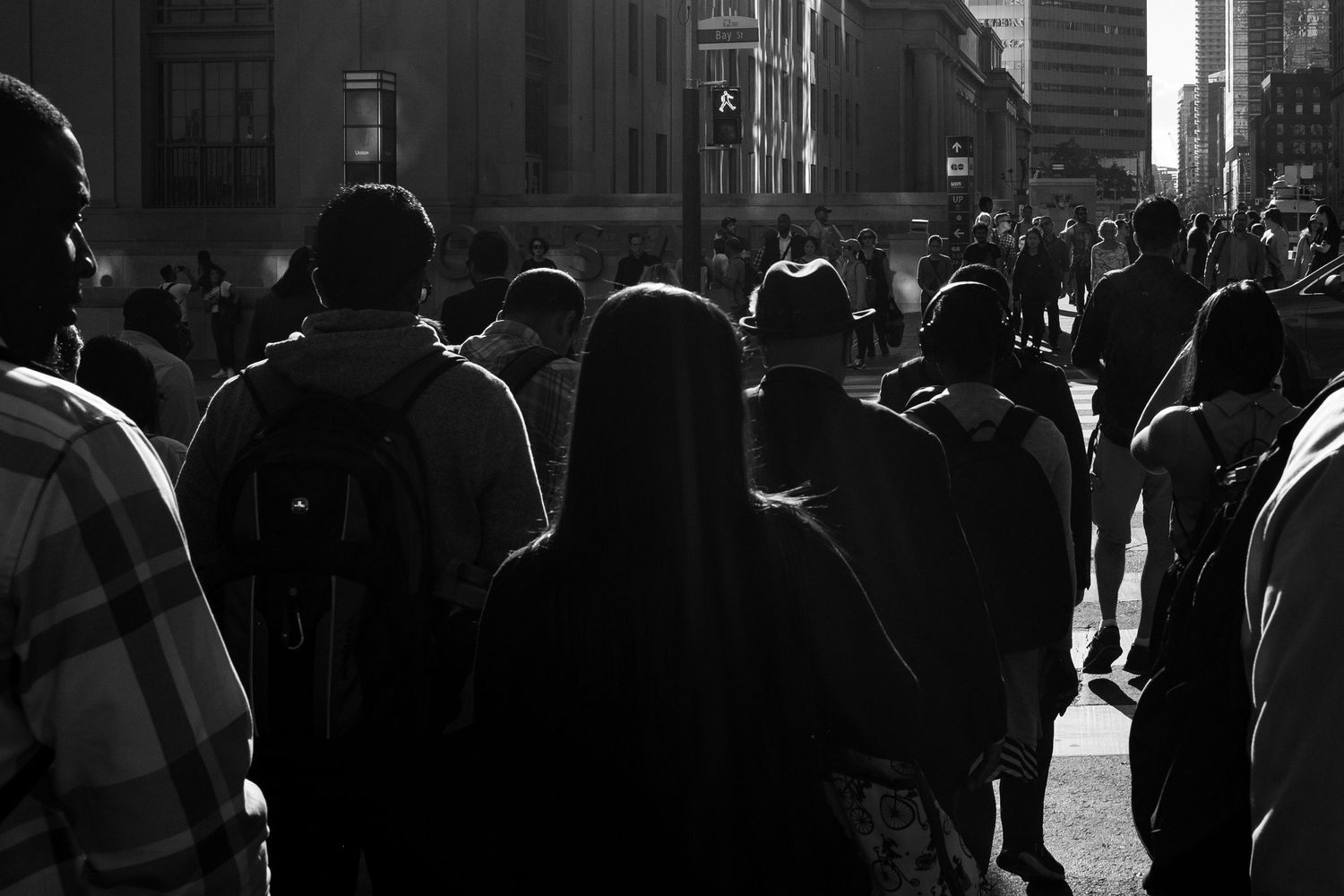 Black and white photo of a crowd of people walking on a busy urban street with tall buildings in the background.
