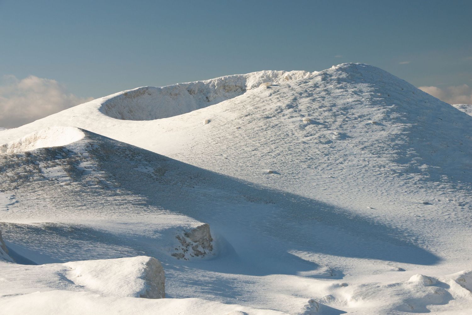 Snow-covered mountain peak with a volcanic crater under a clear blue sky in winter.