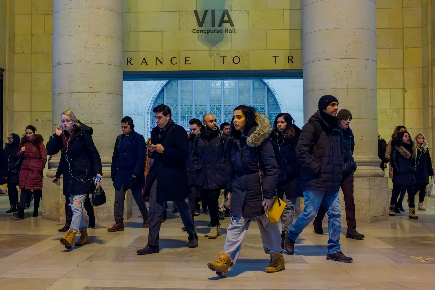 Crowd of people walking through a busy VIA train station entrance in winter coats.