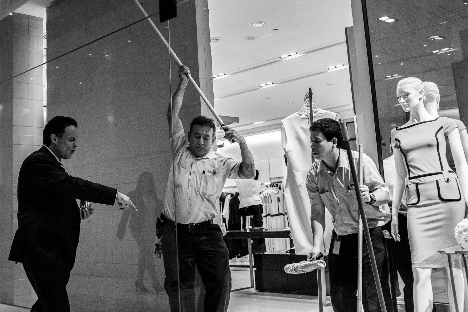 Black and white photo of workers handling mannequins outside a clothing store window display.