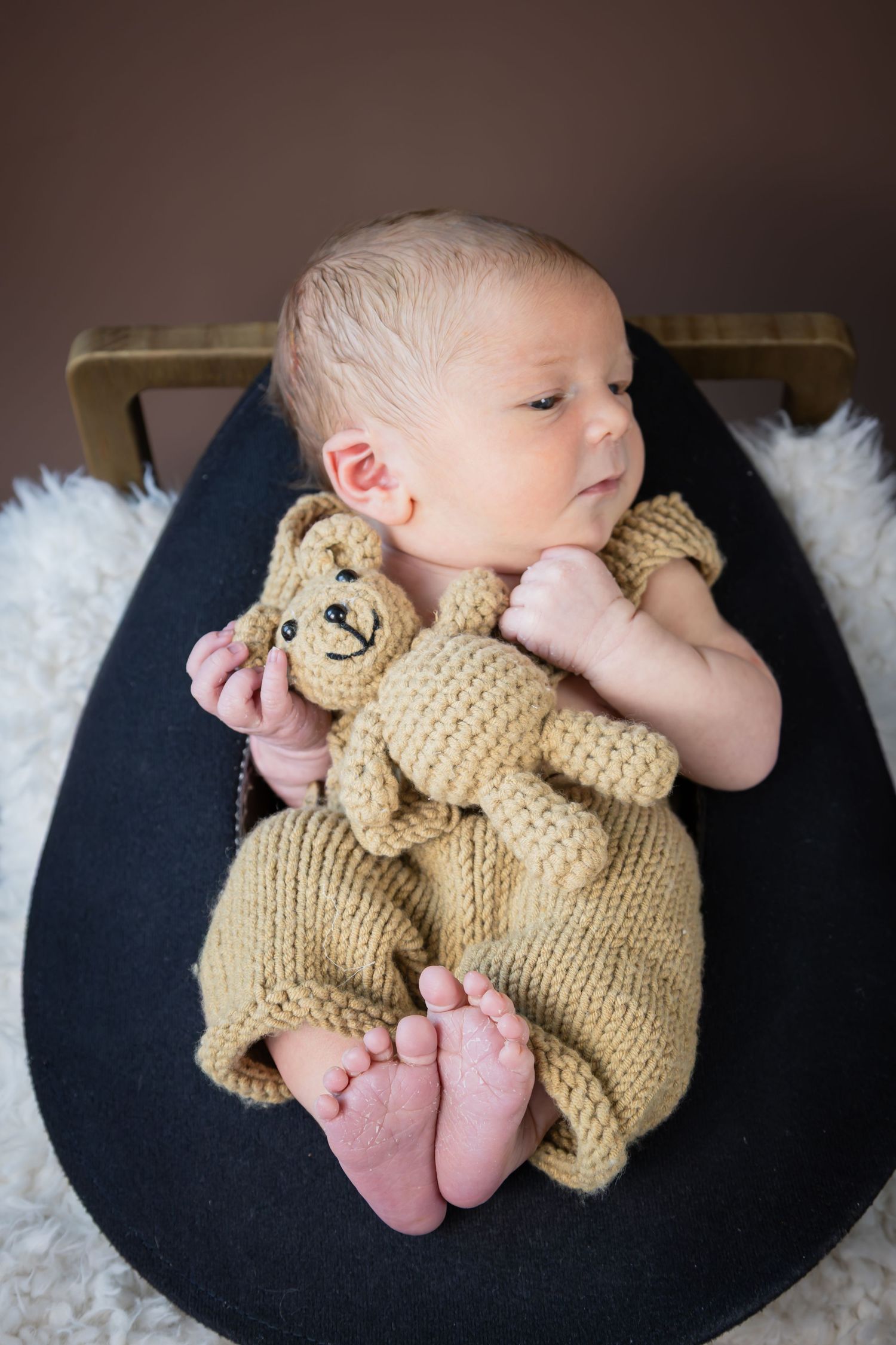 Peaceful newborn baby in knit outfit holding teddy bear toy while resting in small bed.