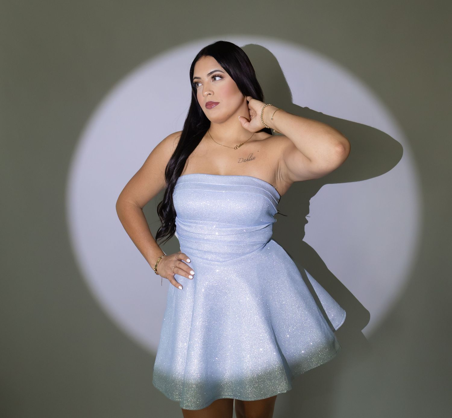 Plus-size woman in strapless blue sparkle mini dress posing in spotlight.