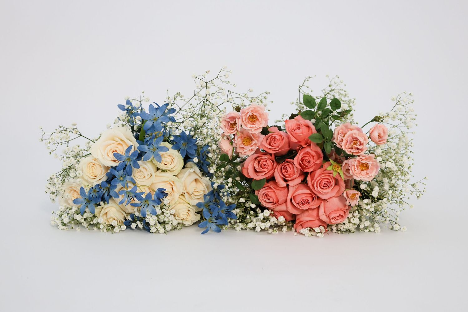Two floral bouquets with roses, baby's breath, and blue delphinium arranged side by side on white background.