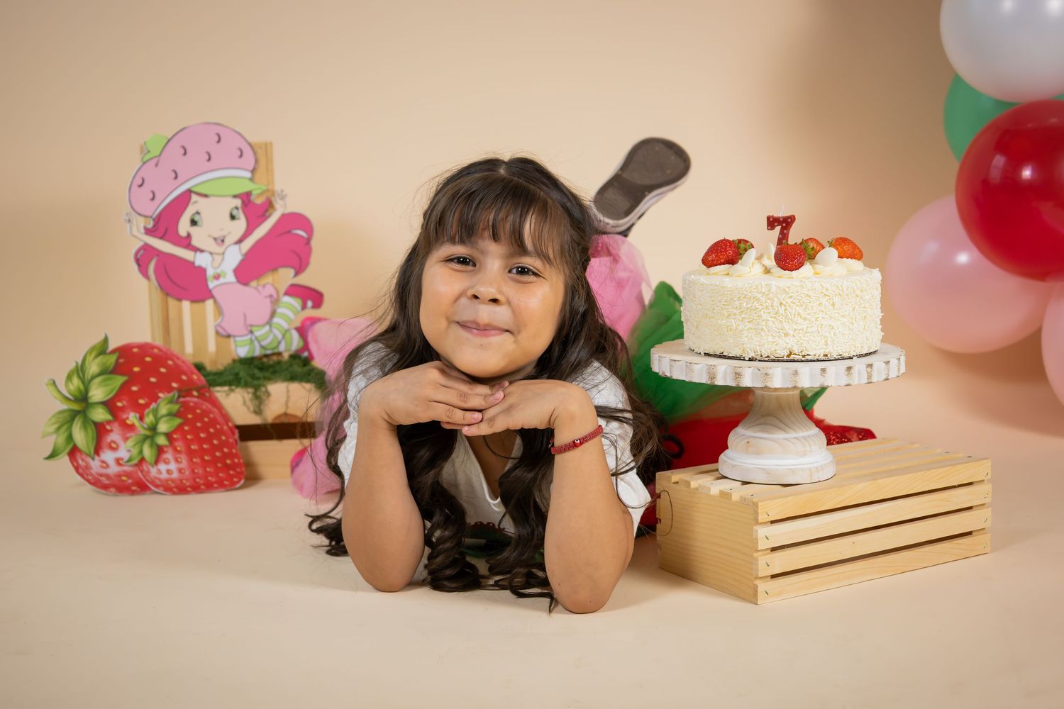 Young girl posing with Strawberry Shortcake themed birthday cake and decorations on her 7th birthday.