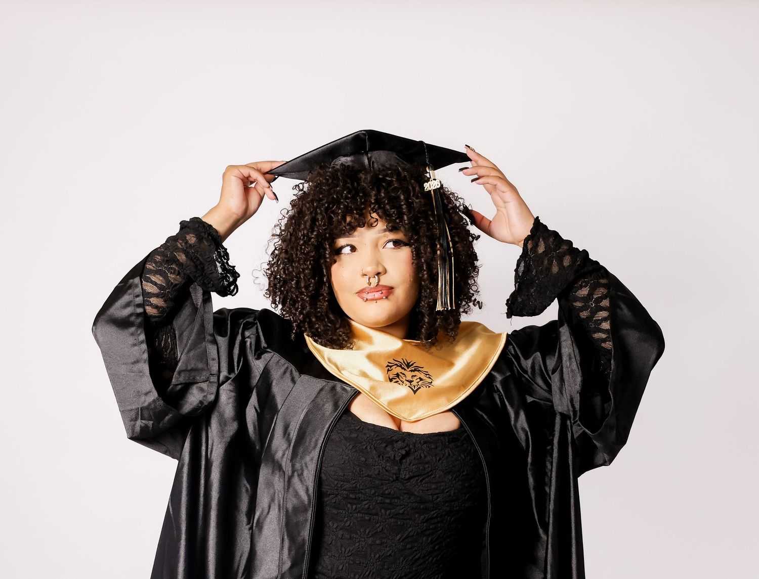 A young woman in black graduation cap and gown with gold hood posing against a white background.