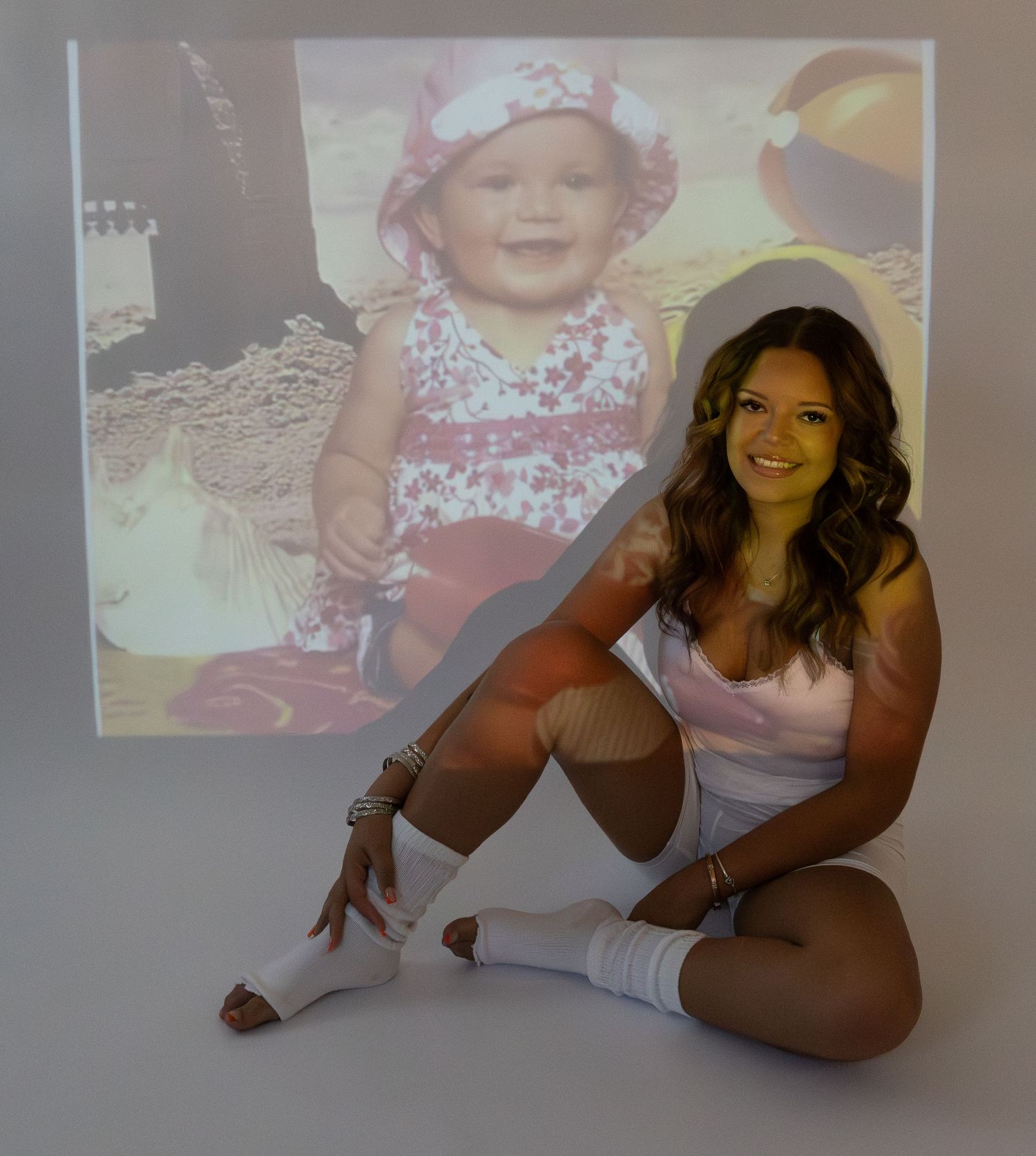Smiling woman sitting before projected baby photo in nostalgic birthday portrait session.