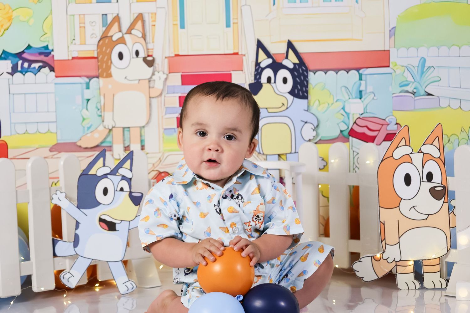 Smiling baby boy sitting in front of a colorful Bluey cartoon themed backdrop with toys.