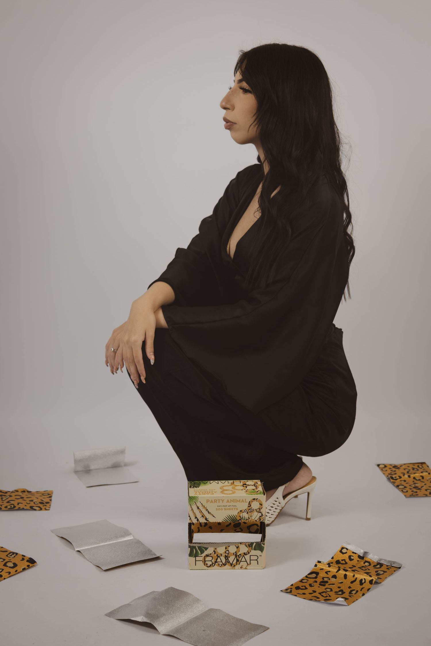 Woman in black outfit crouching beside decorative box with scattered papers on studio floor.