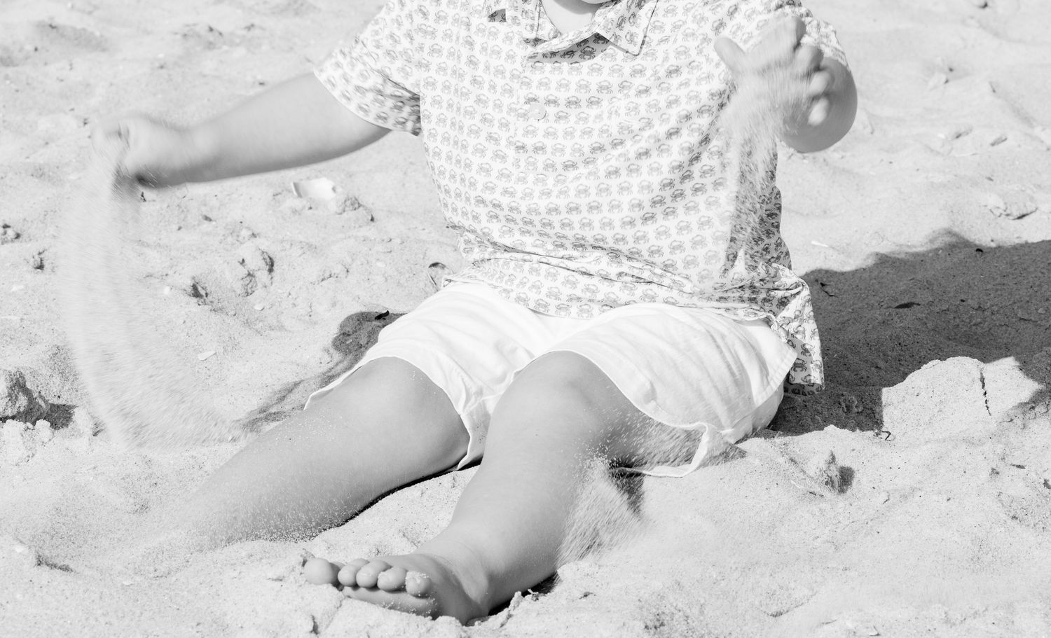 Black and white photo of toddler playing in sand at beach.