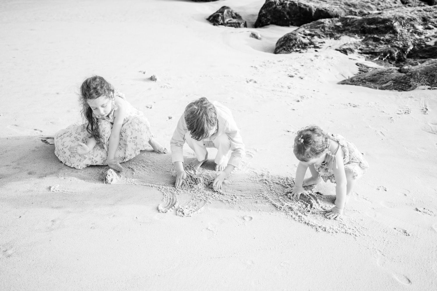 Three children playing in the sand on a beach, building sandcastles together in a black and white photo. child photographer, Hamptons photo