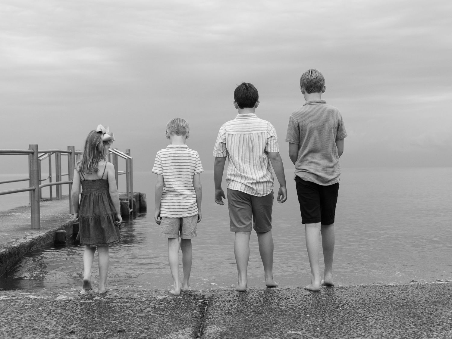 Black and white photo of four children walking barefoot toward the ocean.