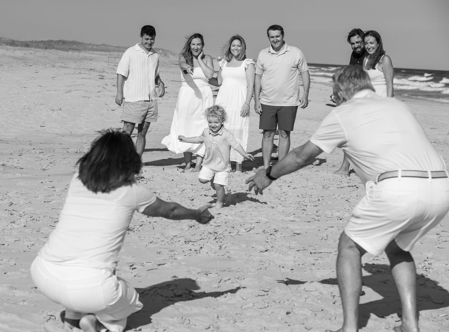 Black and white photo of family playing on beach, two adults crouching as children run toward them.