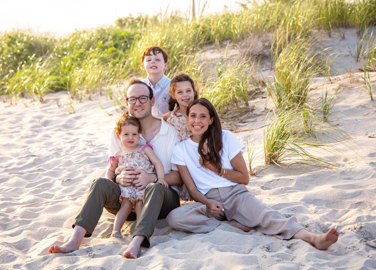 Happy family of five sitting on sandy beach dunes, smiling together on a sunny day. family photographer. Hamptons photographer.beach session