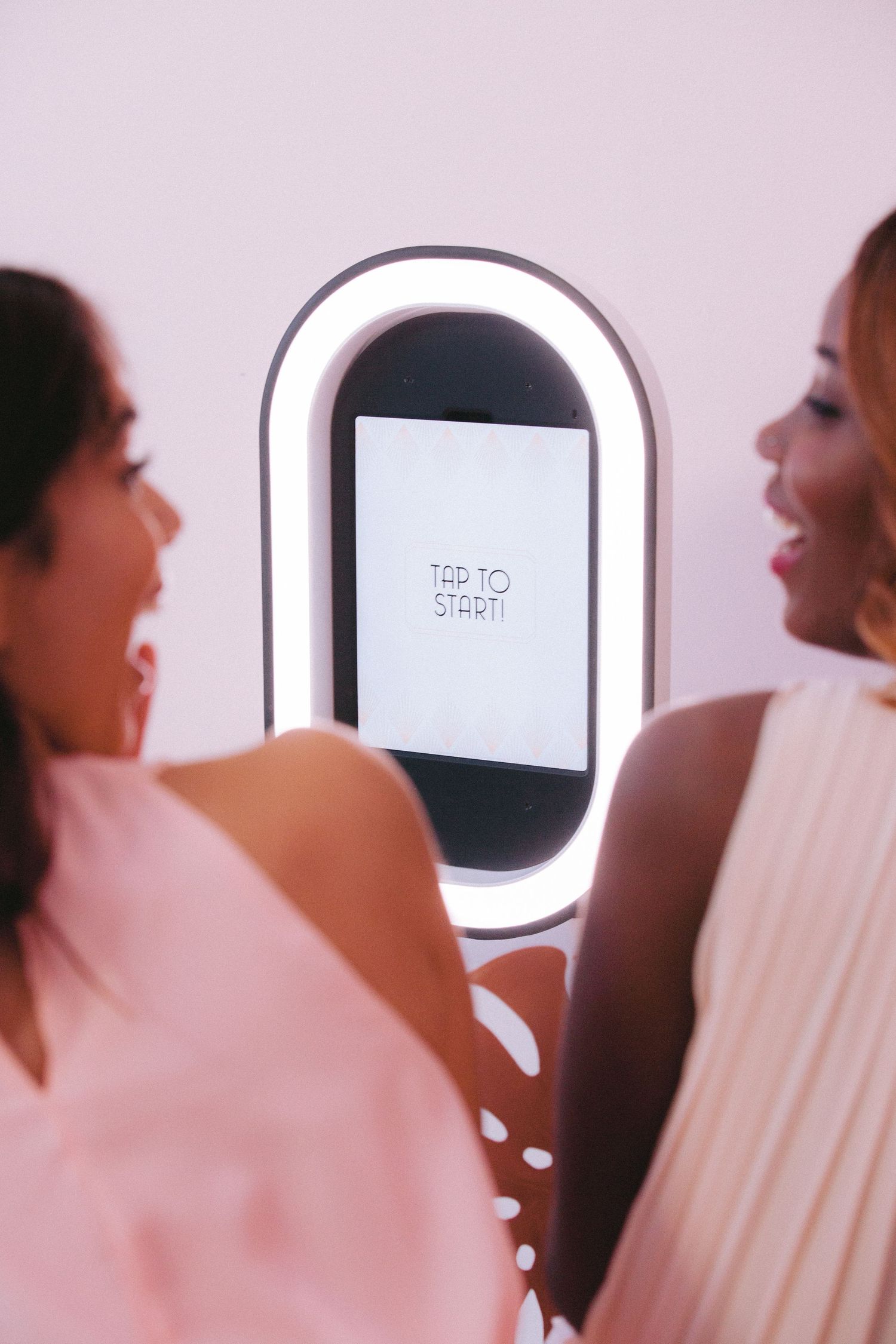Photo booth display with illuminated frame capturing guests in soft pink ambient lighting.
