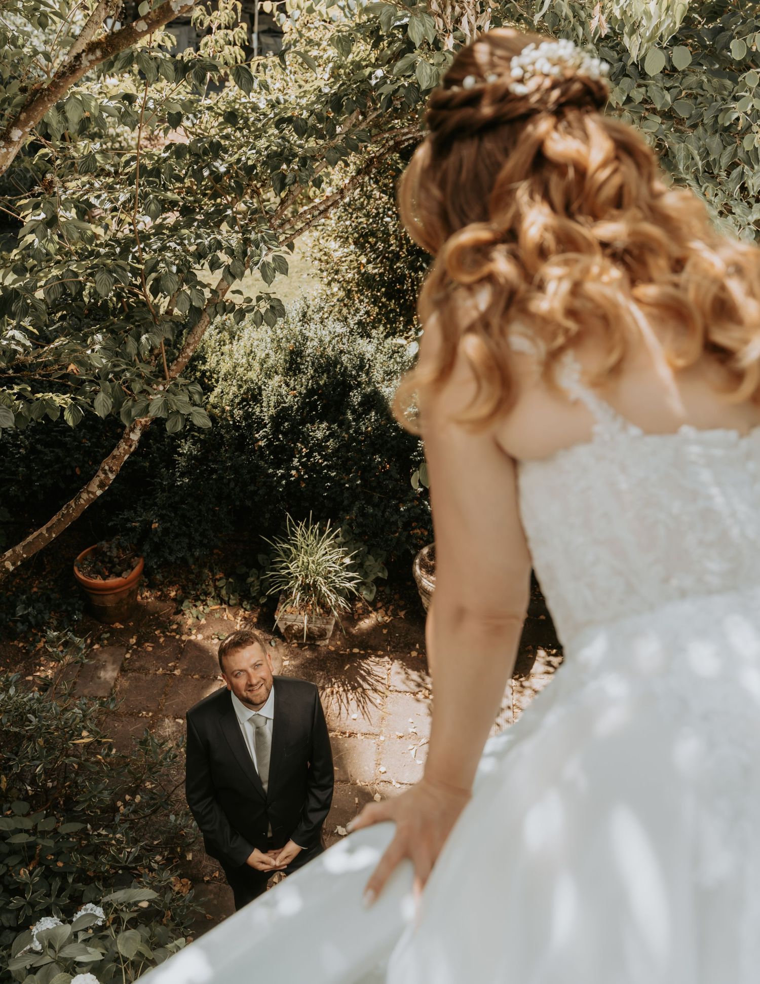 A couple shares a joyful moment during their outdoor garden wedding ceremony under dappled sunlight.