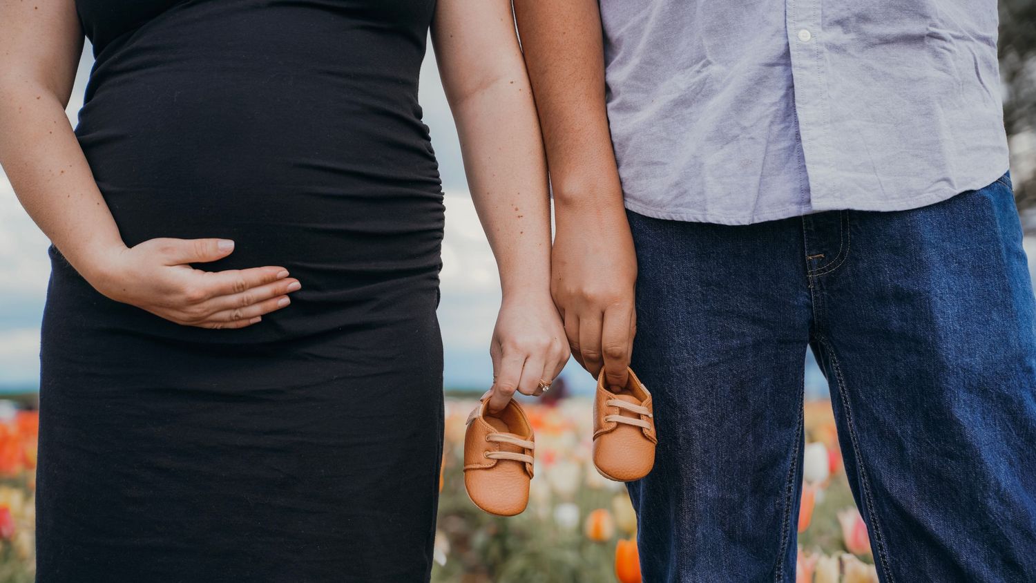 Close up of pregnant woman's belly while holding tiny baby shoes with partner.