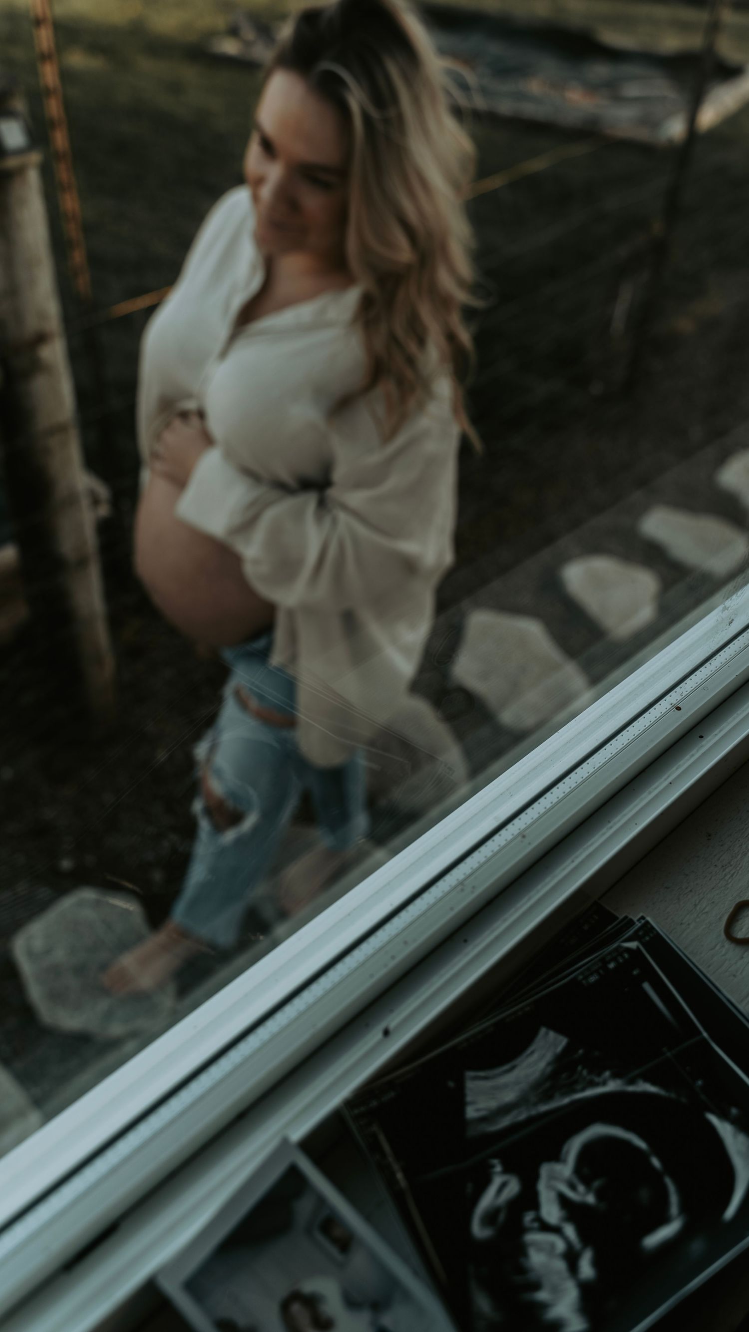 Maternity photo showing expectant mother in white sweater and jeans with ultrasound image visible.