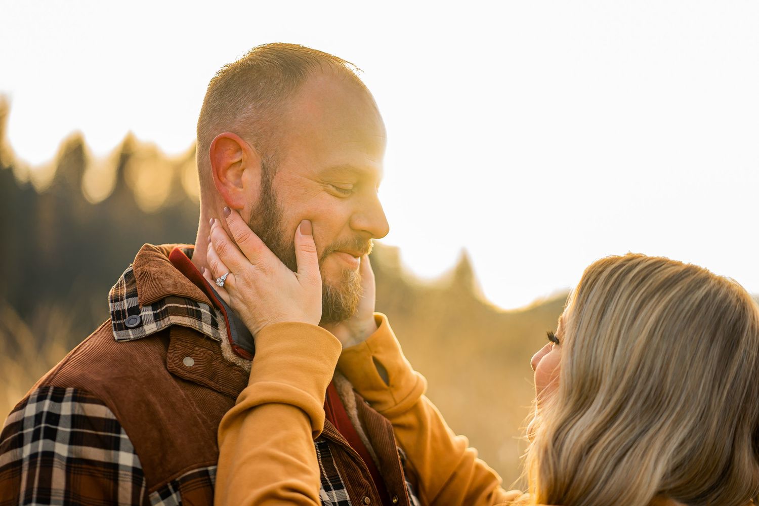 Couple sharing a tender moment outdoors at golden hour, woman gently touching mans bearded face.