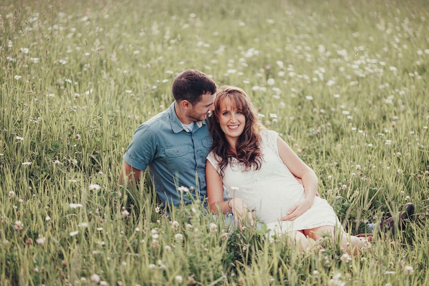 Expecting couple sitting together in a lush green wildflower field during a maternity photo session.