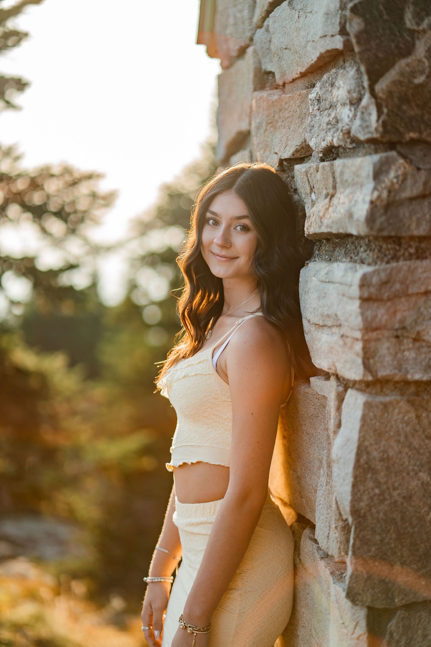 Young woman in yellow outfit leaning against stone wall in golden sunlight.