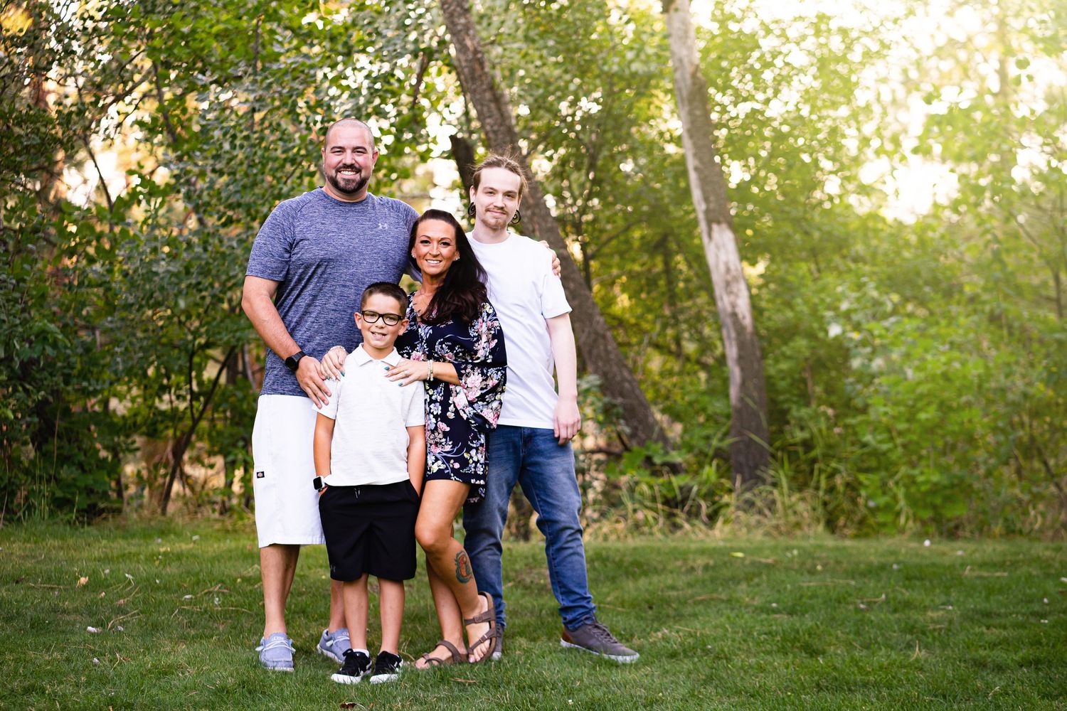 Family of four smiling together on a green lawn with trees in the background.