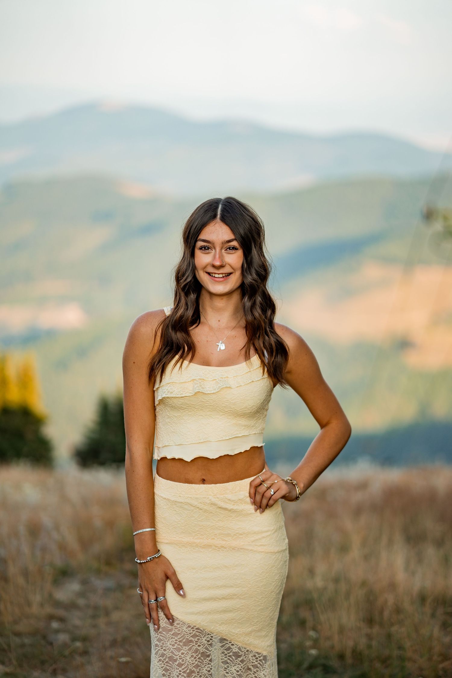Smiling brunette teen in yellow crop top and skirt posing in mountain meadow.
