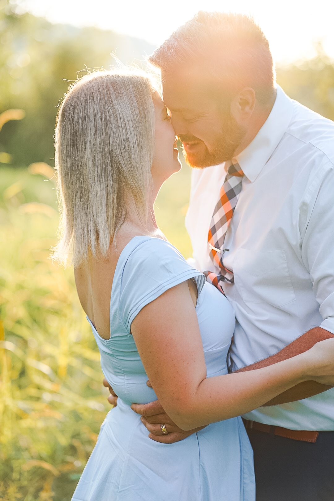 Couple sharing intimate moment backlit by golden sunset in summer meadow field.