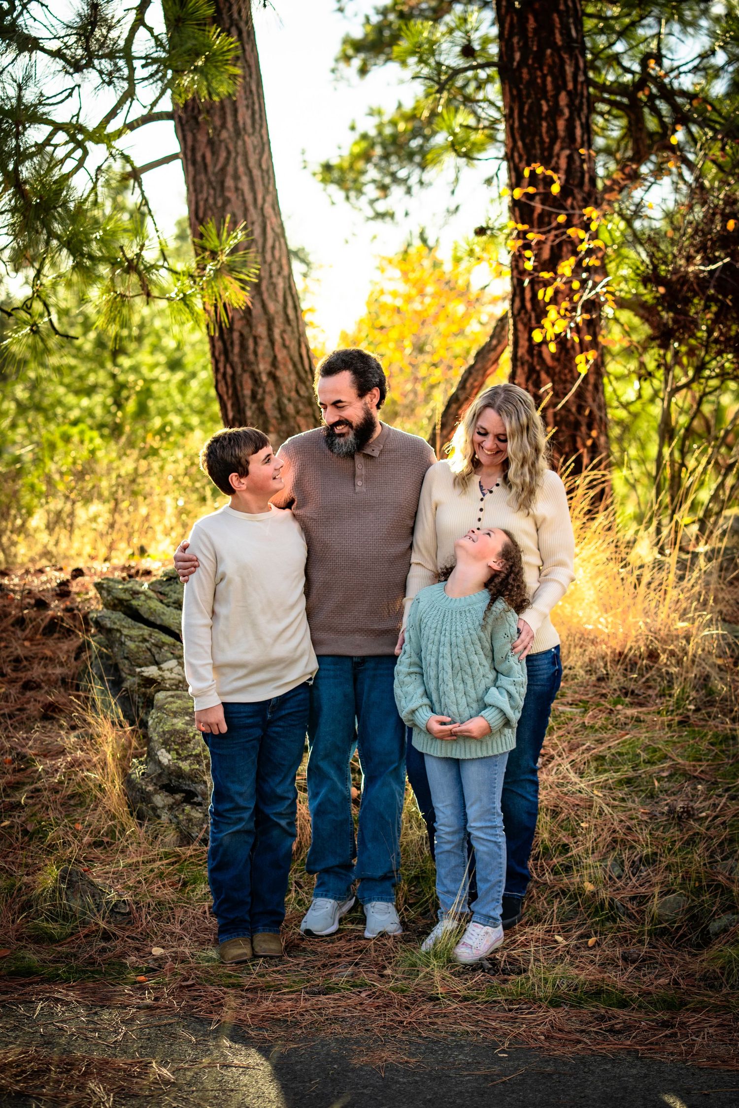 Family of four sharing joyful moment among pine trees in golden autumn forest setting.
