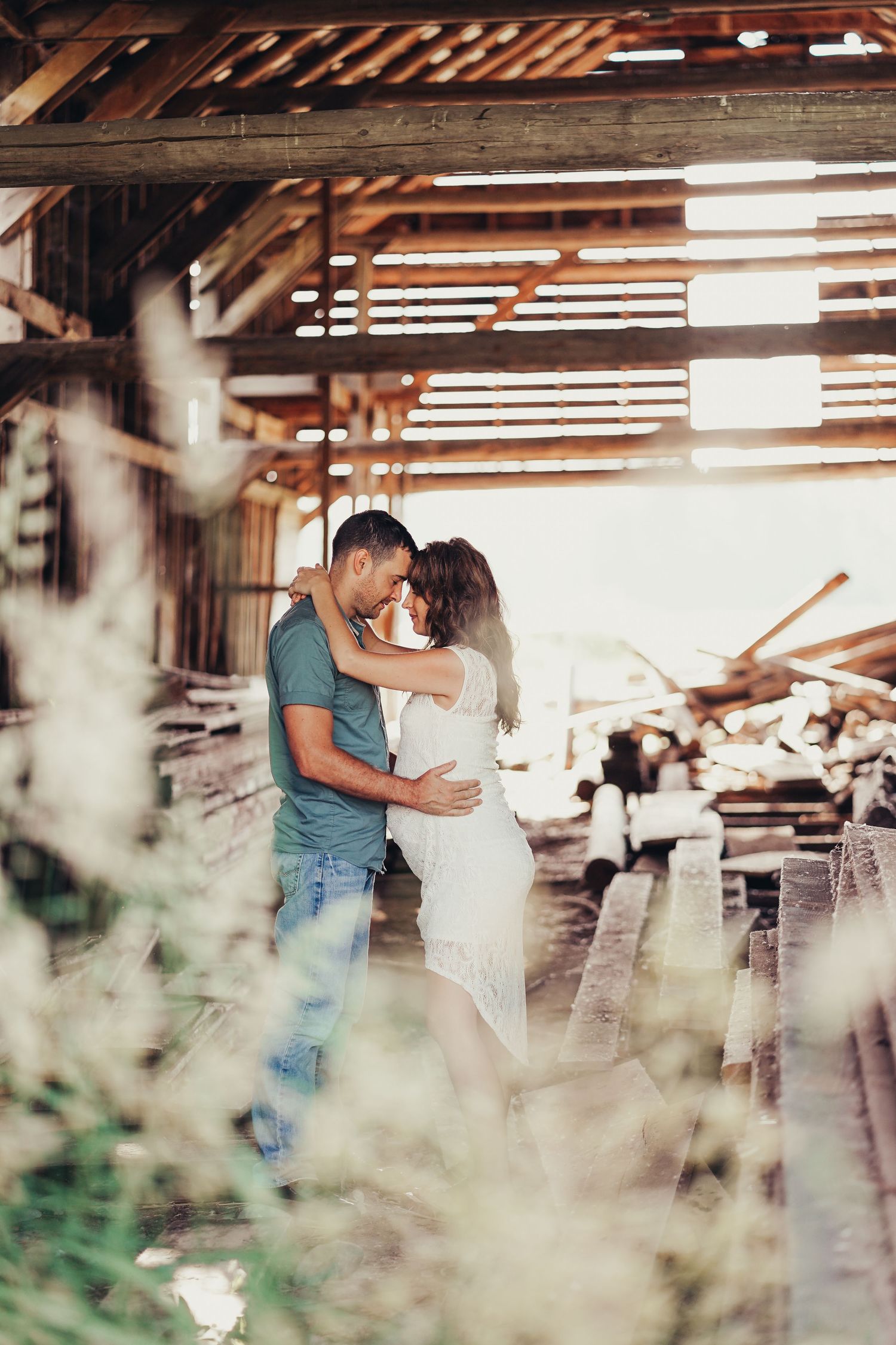 Couple embracing tenderly in a rustic wooden barn with warm sunlight streaming through the slats.