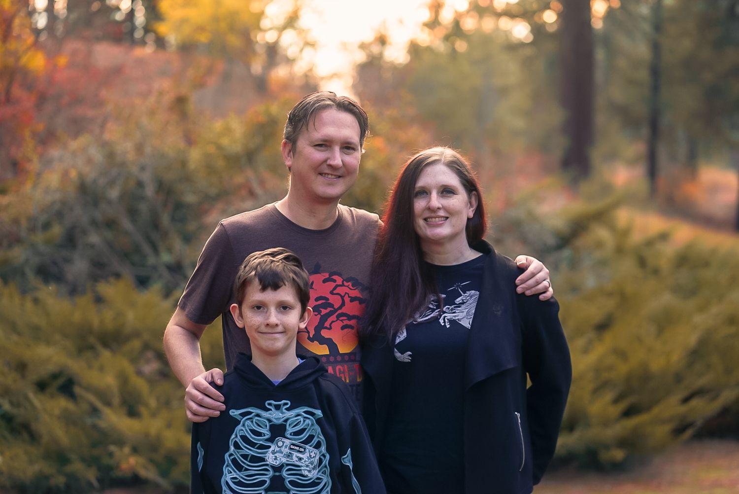 Family of three posing together on a forest path surrounded by colorful fall foliage.