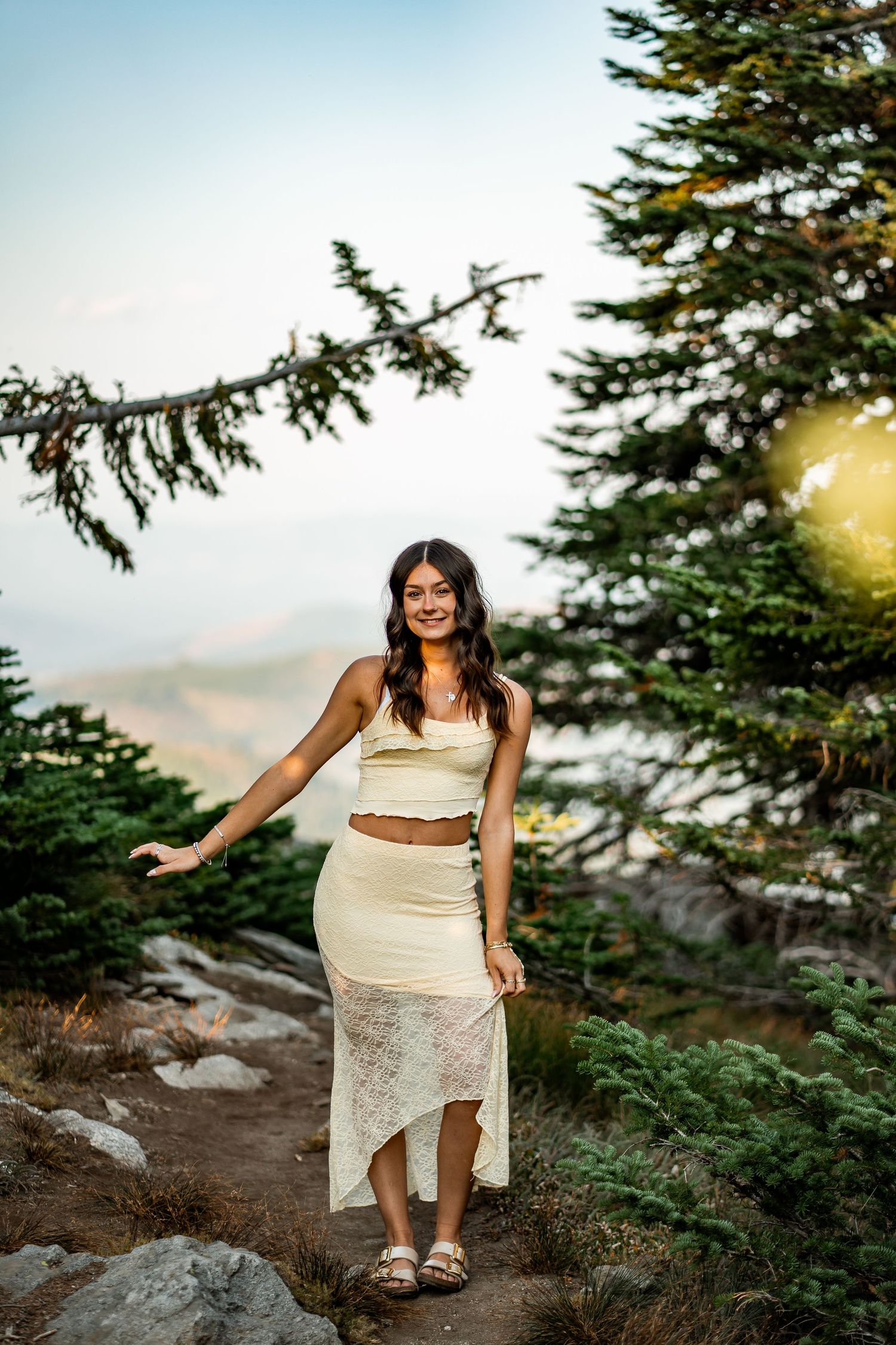 Young woman in cream crop top and lace skirt posing on a mountain trail.
