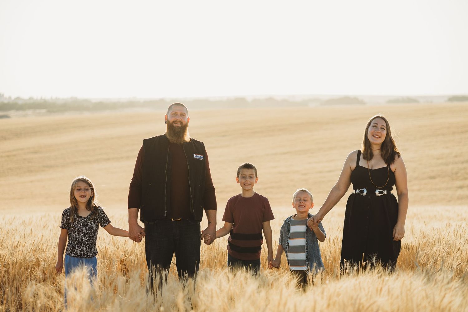 Family of five holding hands while walking through a vast golden wheat field.