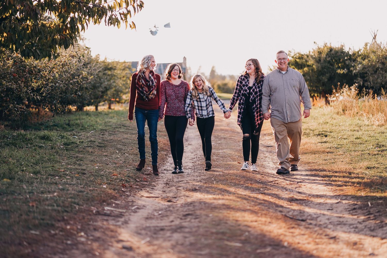 Happy family of five walking hand-in-hand down a sunny rural dirt path in fall.