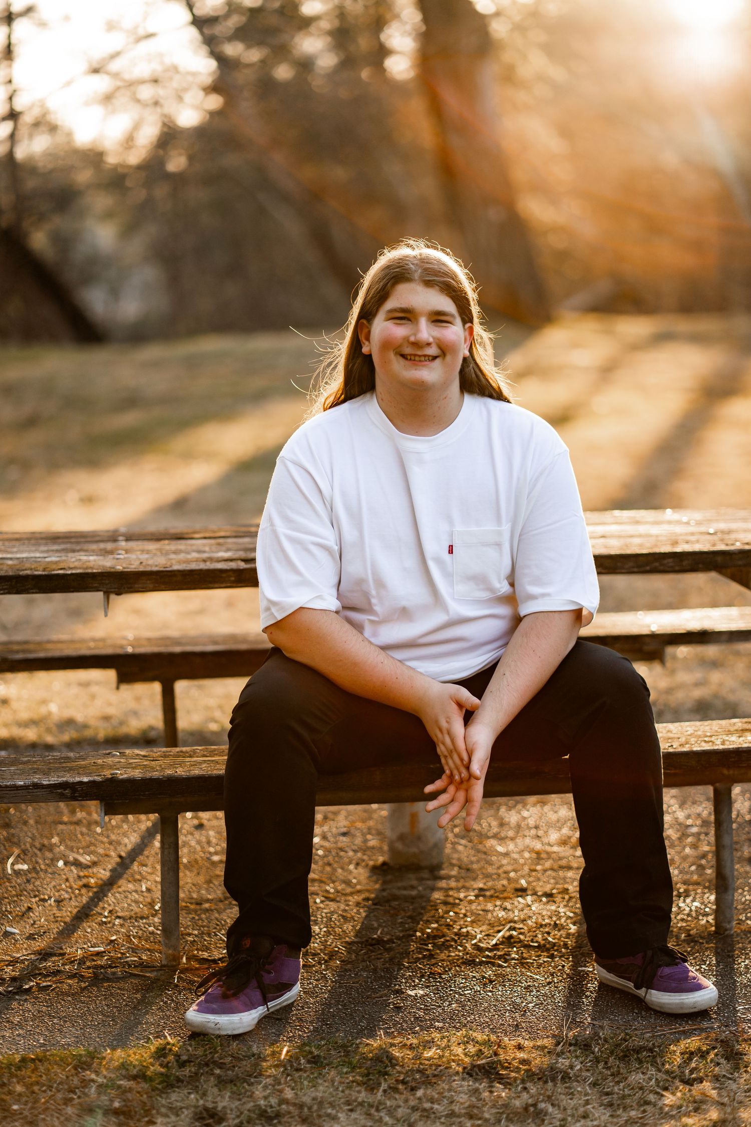 Smiling teen with long hair sitting on bleachers in warm golden sunset light.