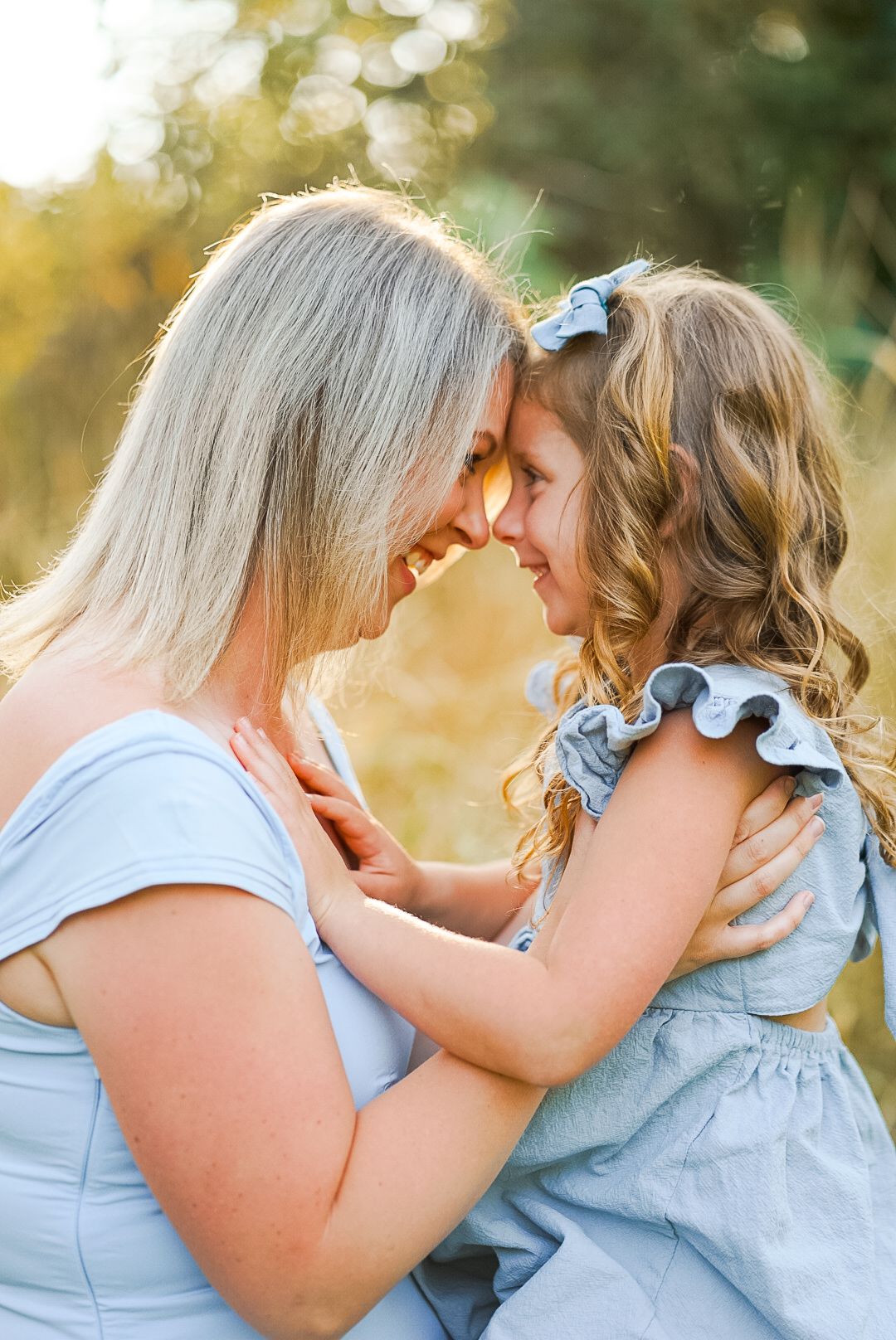Mother and young daughter touching foreheads smiling in tender outdoor moment at golden hour.