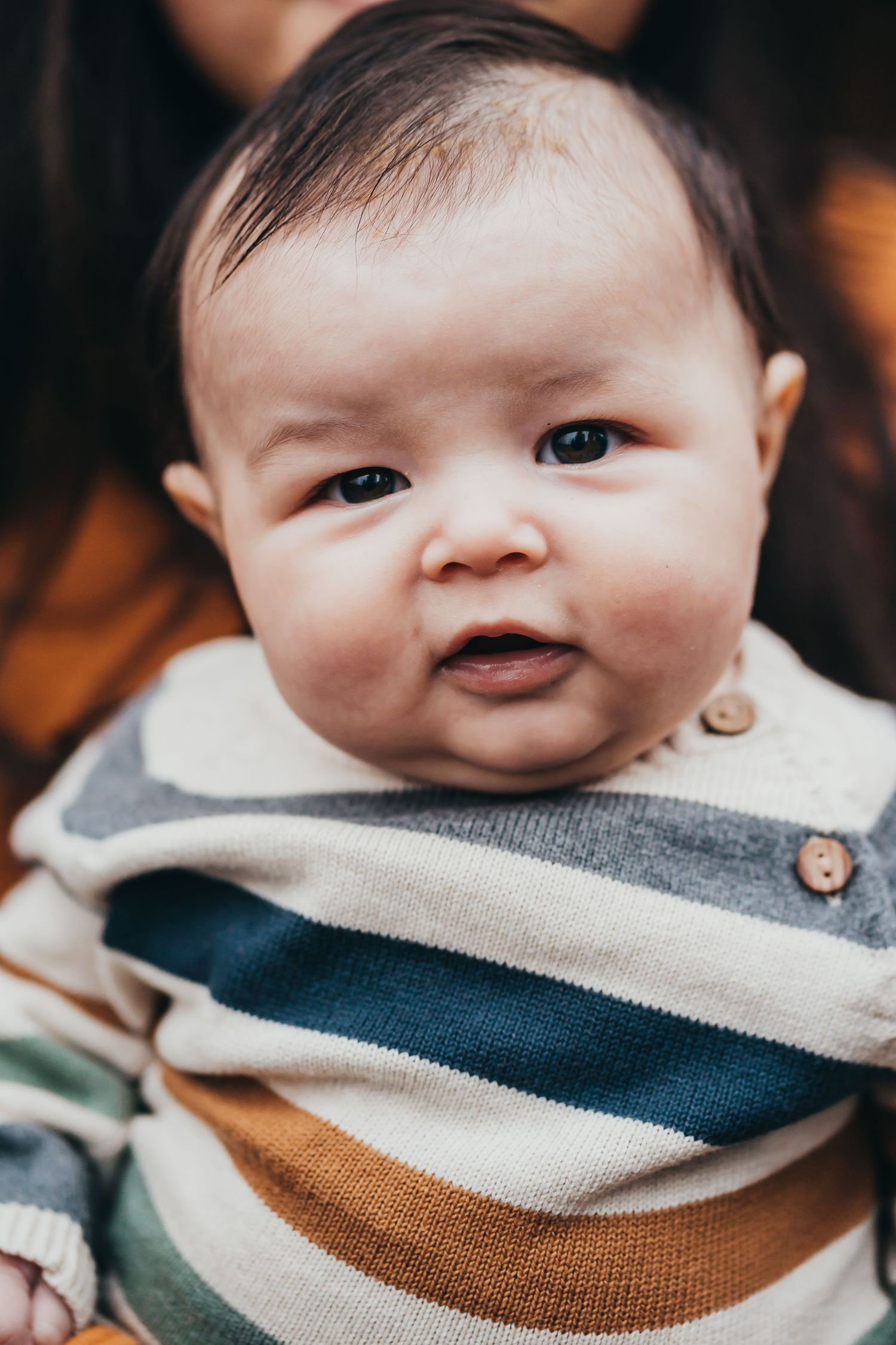 Adorable baby in striped sweater with button details looking curiously at the camera.
