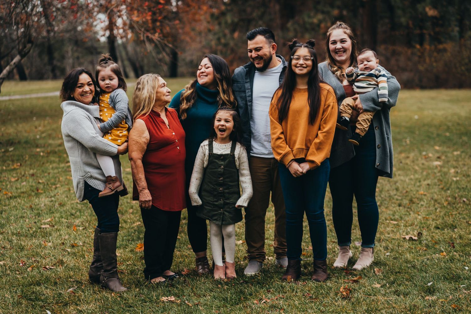 Large multigenerational family group smiling together on a grassy lawn in fall foliage.