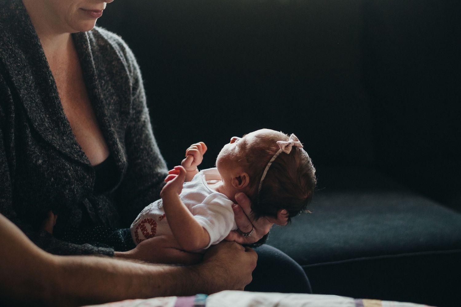 Parent holding a peaceful newborn baby in a white outfit and pink headband.
