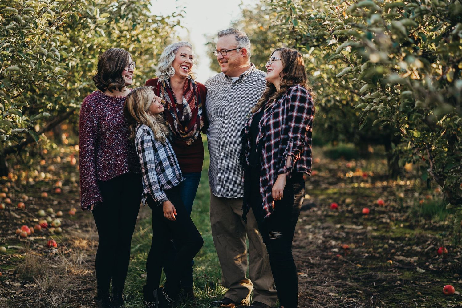 Family of five laughing together in a sunlit apple orchard during an autumn family portrait session.